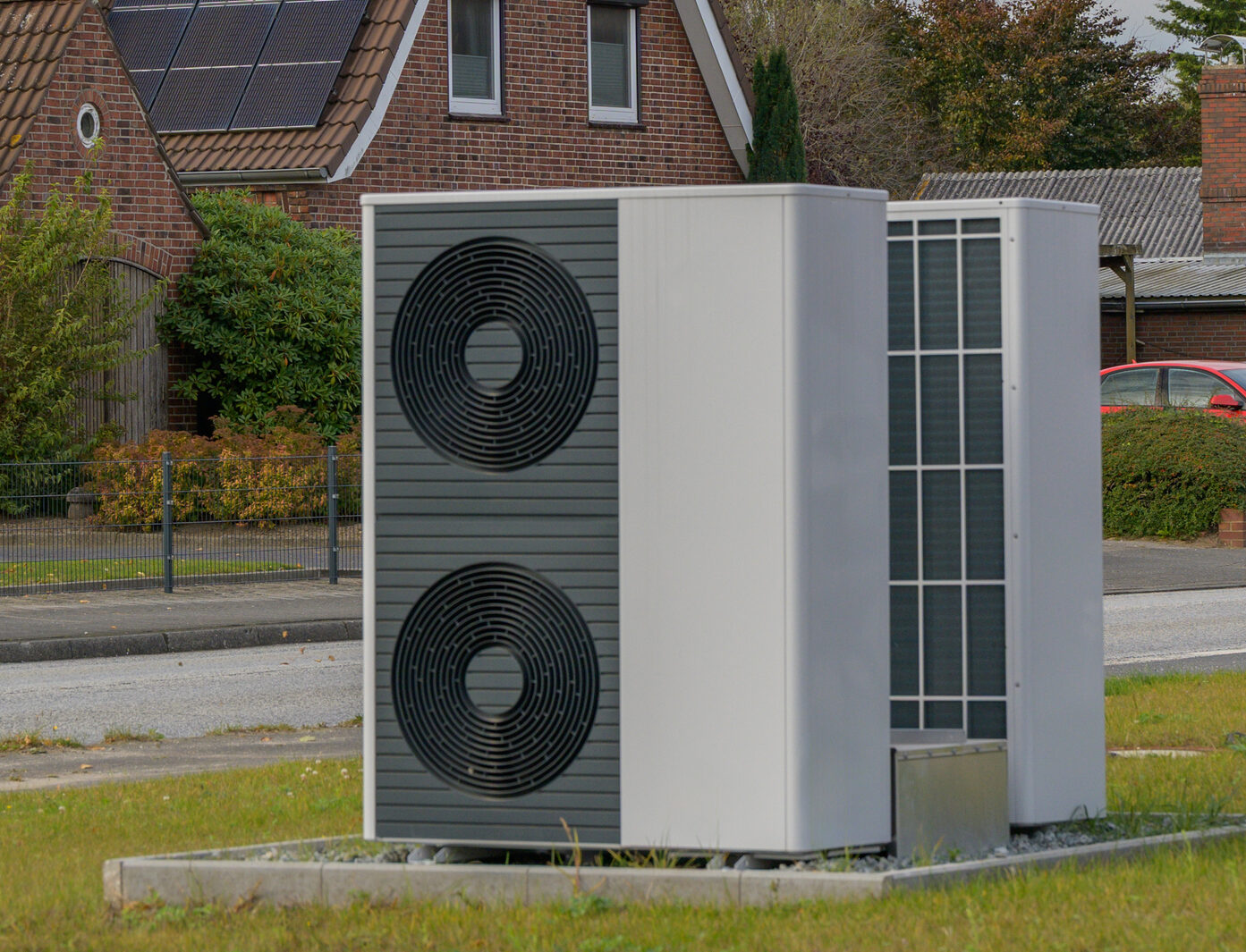 Eine moderne Luft-Wasser-Wärmepumpe steht vor einem Gebäude mit Photovoltaik auf dem Dach. Diese Kombination macht eine neue Wärmepumpe im Mehrfamilienhaus wirtschaftlich rentabel.