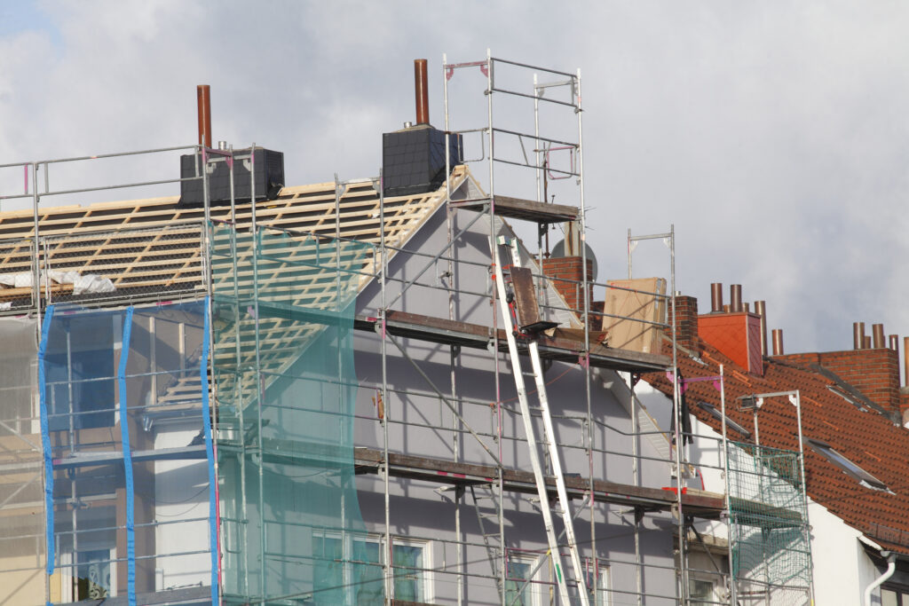 Eingerüstetes Mehrfamilienhaus während einer umfassenden Dachsanierung, vorbereitend für die Installation einer Photovoltaikanlage.